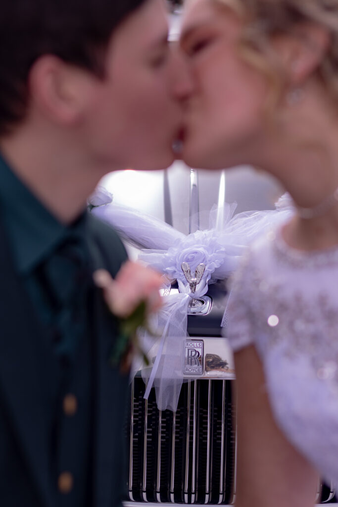 Newlyweds kissing in front of their wedding Rolls Royce.