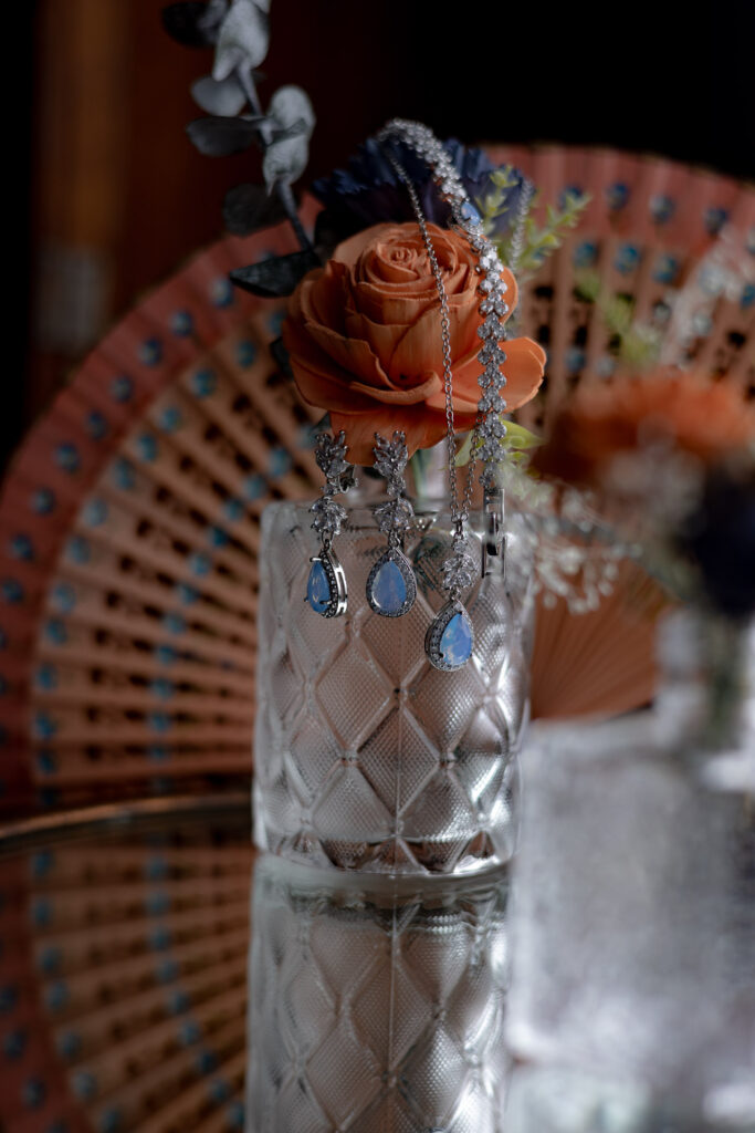 Simple blue wedding jewelry highlighted against an orange rose and fan.