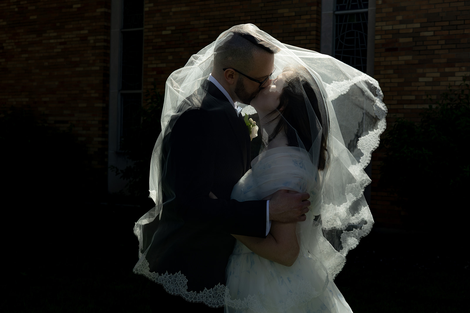 Catholic Couple tenderly kisses under the veil as the breeze picks up.
